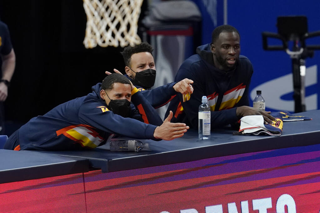 Golden State Warriors forward Juan Toscano-Anderson, from left, watches with guard Stephen Curry and forward Draymond Green against the Philadelphia 76ers during an NBA basketball game in San Francisco, Tuesday, March 23, 2021. (AP Photo/Jeff Chiu)