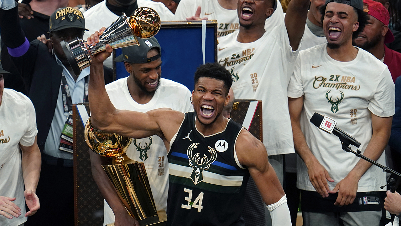 Milwaukee Bucks forward Giannis Antetokounmpo (34) reads with the championship trophy after defeating the Phoenix Suns in Game 6 of basketball's NBA Finals in Milwaukee, Tuesday, July 20, 2021. The Bucks won 105-98. (AP Photo/Paul Sancya)